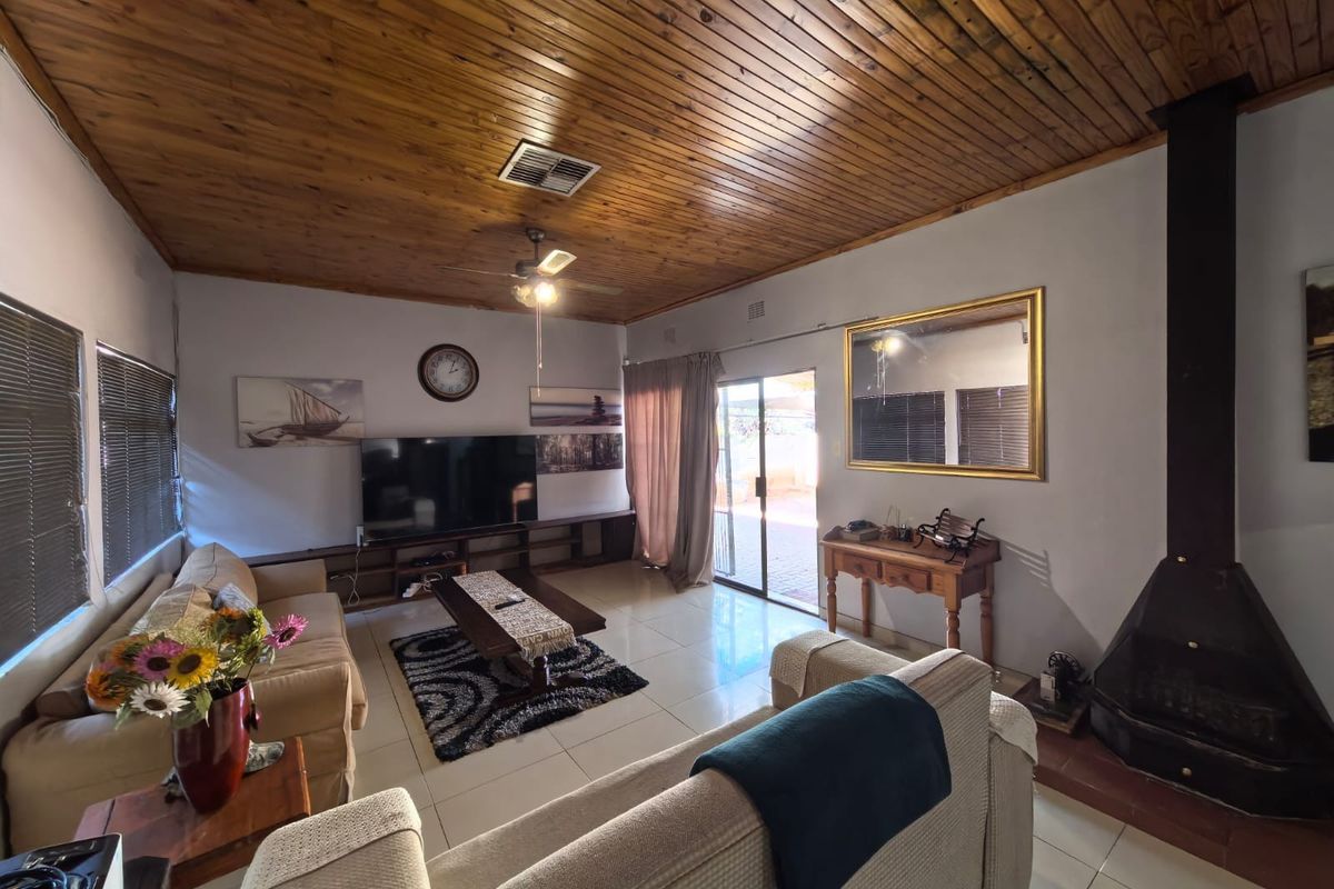 Spacious living room featuring a warm timber-clad ceiling, tiled flooring, and a cozy freestanding fireplace, with direct access to the outdoor area.