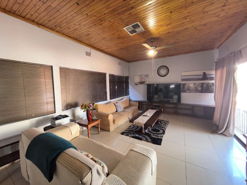 Spacious living room featuring a warm timber-clad ceiling, tiled flooring, and large windows with venetian blinds, offering a comfortable and functional family space.