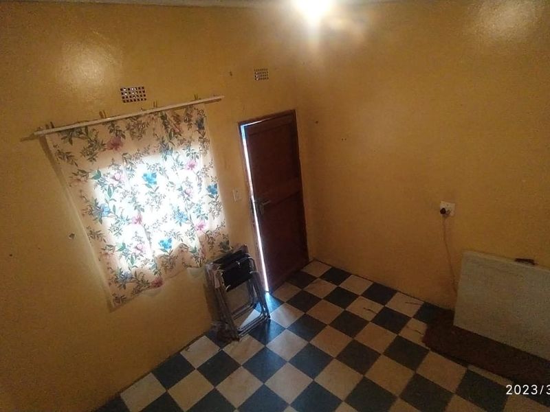 An empty living room featuring checkered floor tiles and a timber door, requiring cosmetic updates to improve its overall appeal.