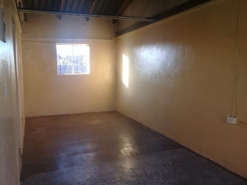 An empty, unfinished room featuring exposed rafters, concrete flooring, and security bars on the window, offering a blank canvas for renovation.