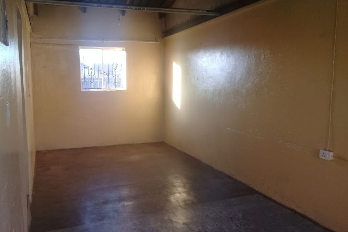 An empty, unfinished room featuring exposed rafters, concrete flooring, and security bars on the window, offering a blank canvas for renovation.