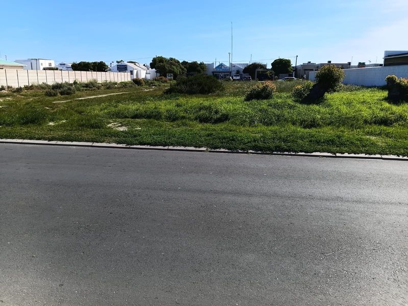 A vacant residential plot featuring a level grassed surface, enclosed by a concrete boundary wall, with direct access to a paved street.