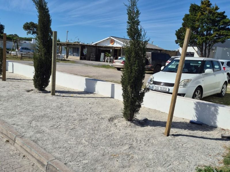 A view of the property frontage featuring a low concrete boundary wall, gravel landscaping, and paved curbing along the street edge.