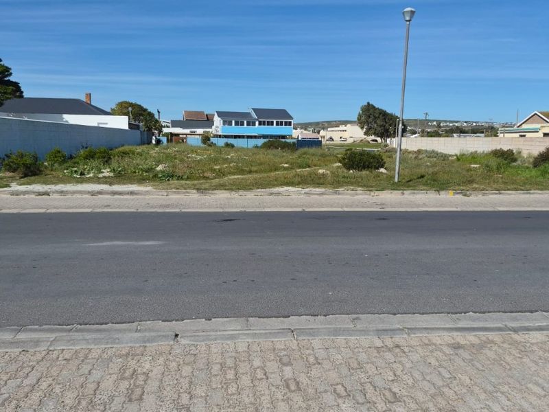 A vacant residential plot of land situated along a paved street with existing boundary walls and street lighting infrastructure.
