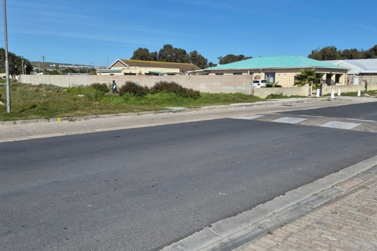 A street-level view of the residential property, showing the paved road, sidewalk, and perimeter boundary wall.