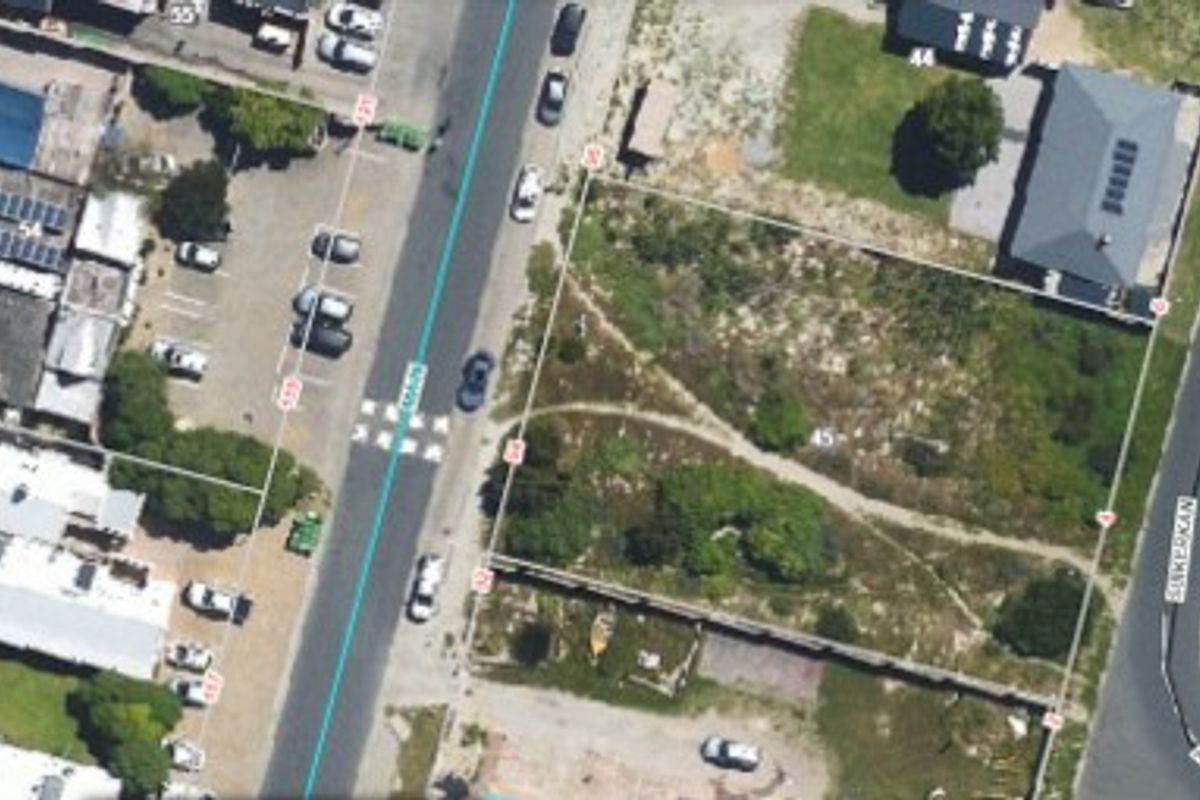 An aerial view of a vacant residential plot situated in a developed neighborhood, showing property boundaries and surrounding street access.