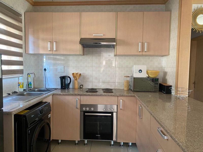 A functional kitchen featuring light wood-finish cabinetry, granite countertops, a built-in oven with hob, and an integrated extractor fan.
