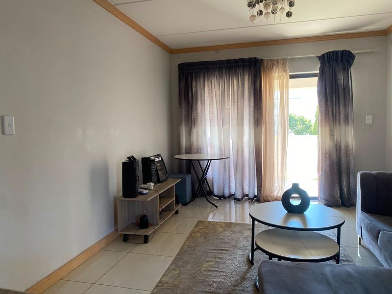 A living room featuring tiled flooring, neutral walls, and a sliding glass door providing access to an outdoor area.