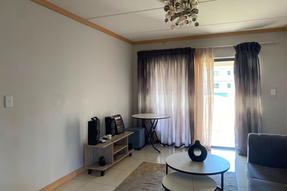 A living room featuring tiled flooring, a modern ceiling light fixture, and a sliding glass door providing access to the exterior.