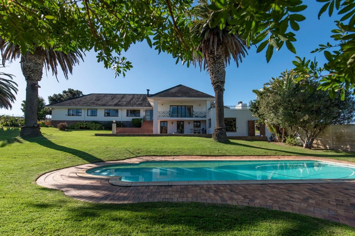 Rear view of the farm property featuring a well-maintained swimming pool, brick paved surround, expansive lawn, and a two-story residence with a balcony.
