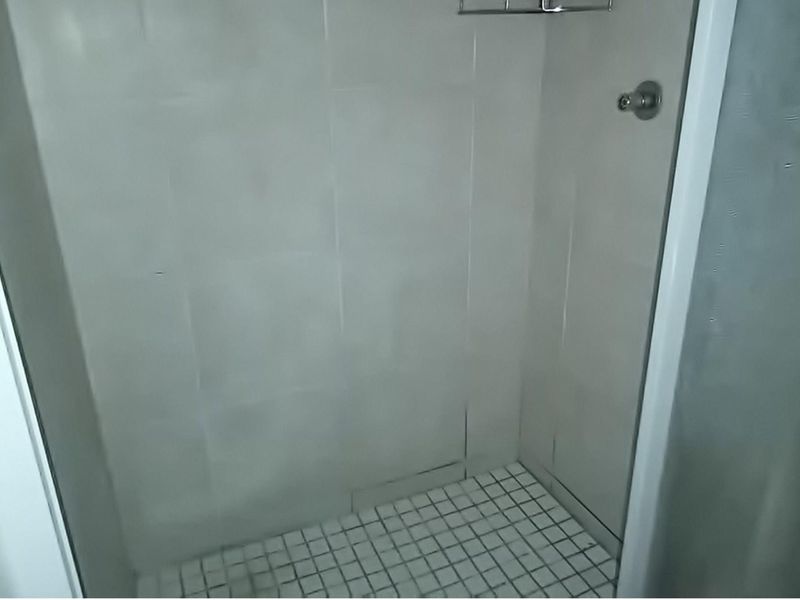A compact shower stall featuring tiled walls and flooring, equipped with a standard shower mixer and integrated caddy.