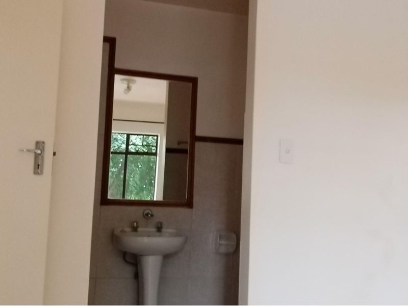 A compact bathroom featuring a pedestal basin, wall-mounted mirror, and tiled splashback, viewed through a doorway.