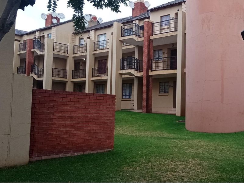 Exterior view of a multi-story apartment complex featuring private balconies, brick accents, and a shared garden area.