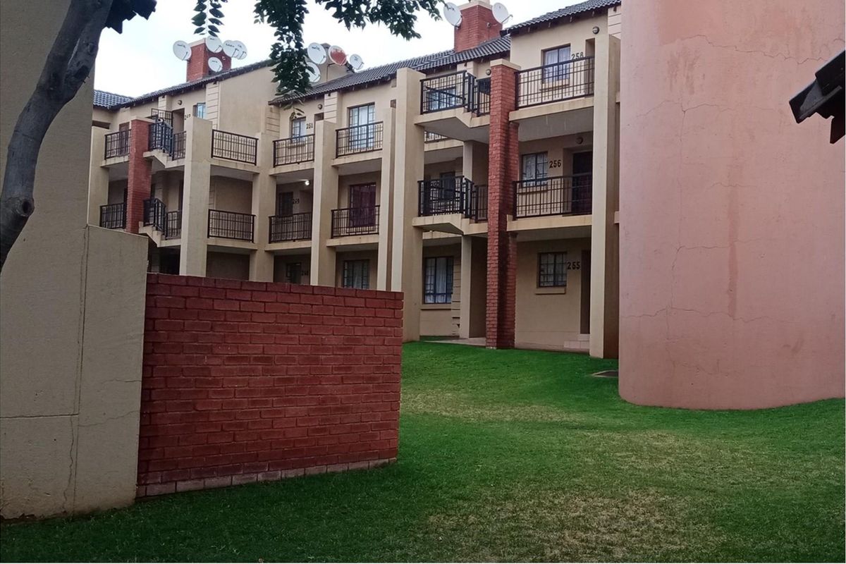 Exterior view of a multi-story apartment complex featuring private balconies, brick accents, and a shared garden area.