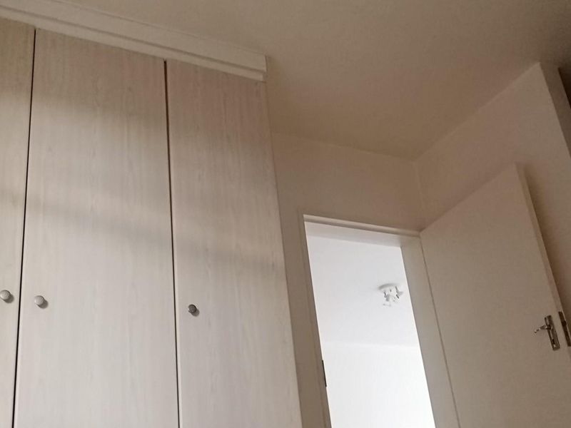 A view of a bedroom interior featuring built-in cupboards with light wood-grain finish and a standard internal door leading to an adjacent space.