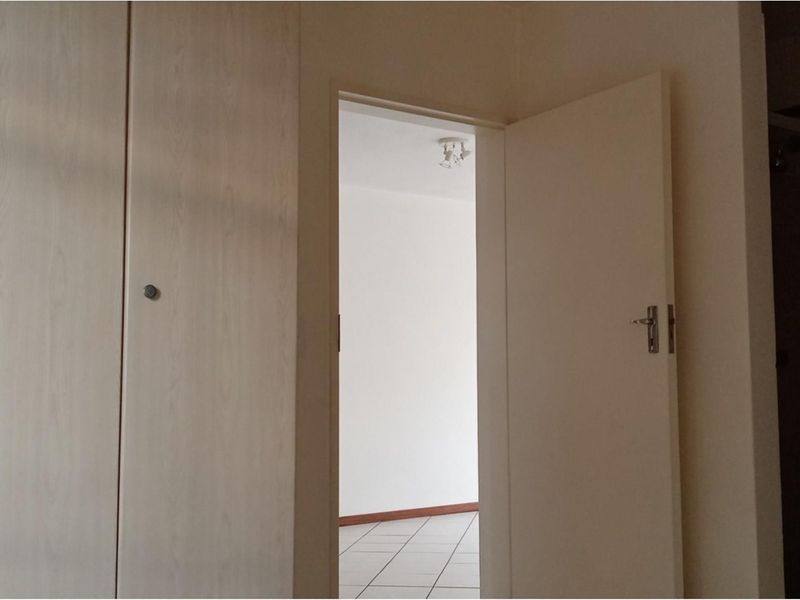 A view through an open doorway into a tiled room, featuring built-in cupboards in the hallway area.