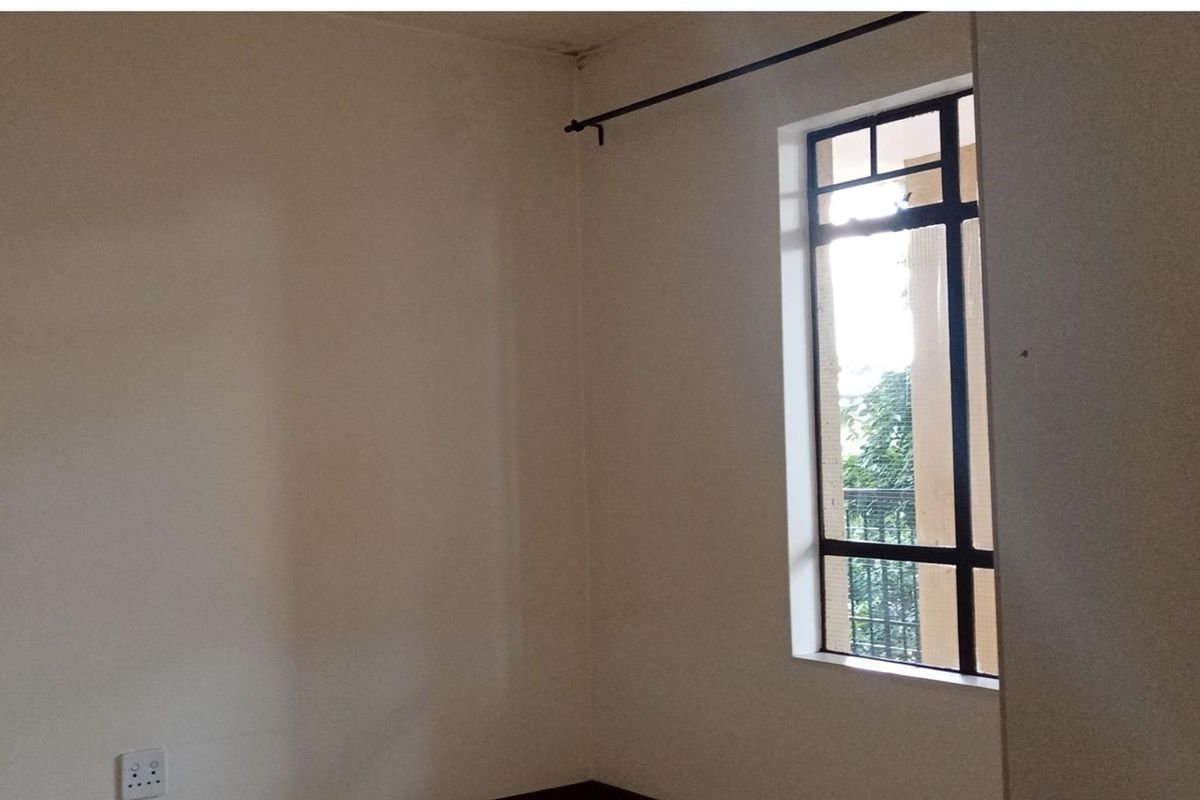 An empty bedroom featuring a metal-framed window and a curtain rod, showing signs of ceiling water damage.