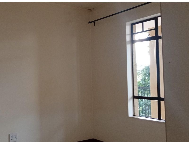 An empty bedroom featuring a metal-framed window and a curtain rod, showing signs of ceiling water damage.