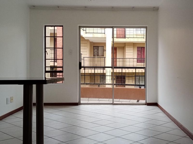 An empty living area featuring tiled flooring, a sliding glass door leading to a balcony, and security bars on the windows.