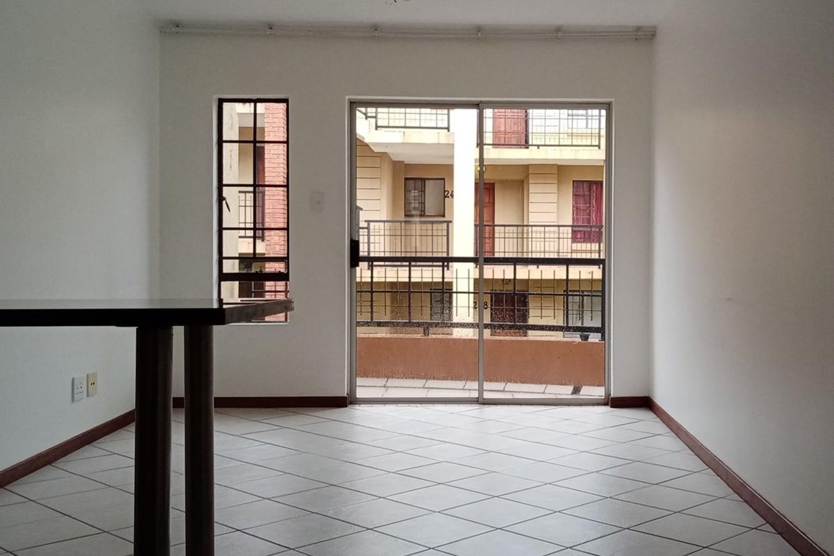An empty living area featuring tiled flooring, a sliding glass door leading to a balcony, and security bars on the windows.