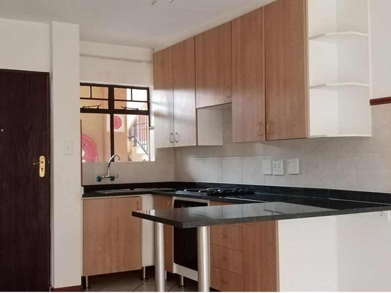 A functional kitchen featuring light wood-finish cabinetry, dark granite countertops, a built-in hob and oven, and a convenient breakfast bar area.
