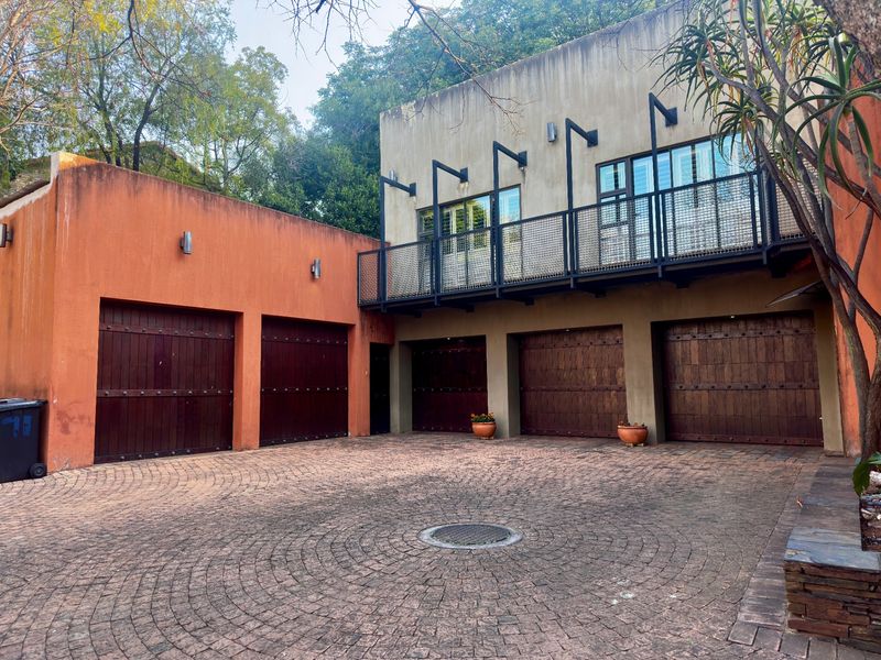 Spacious exterior front view featuring a large cobblestone driveway, five timber garage doors, and an upper-level balcony with metal railings.