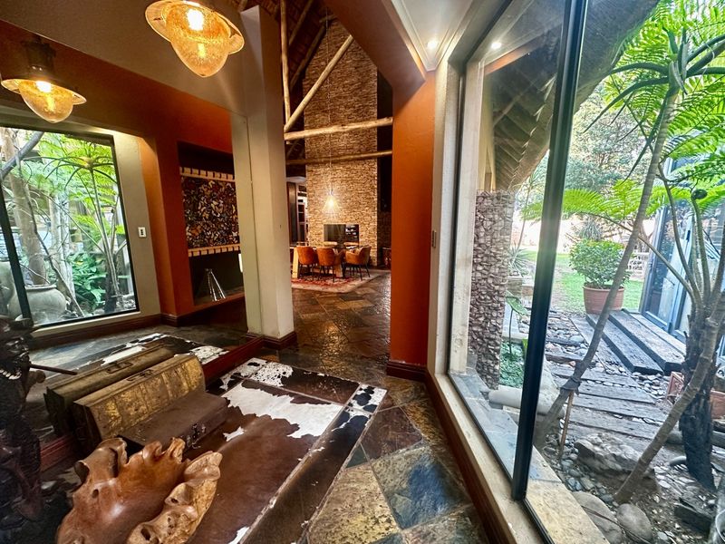 Spacious living area featuring natural slate flooring, exposed timber trusses, a striking stone feature wall, and large glass doors opening to a lush garden.