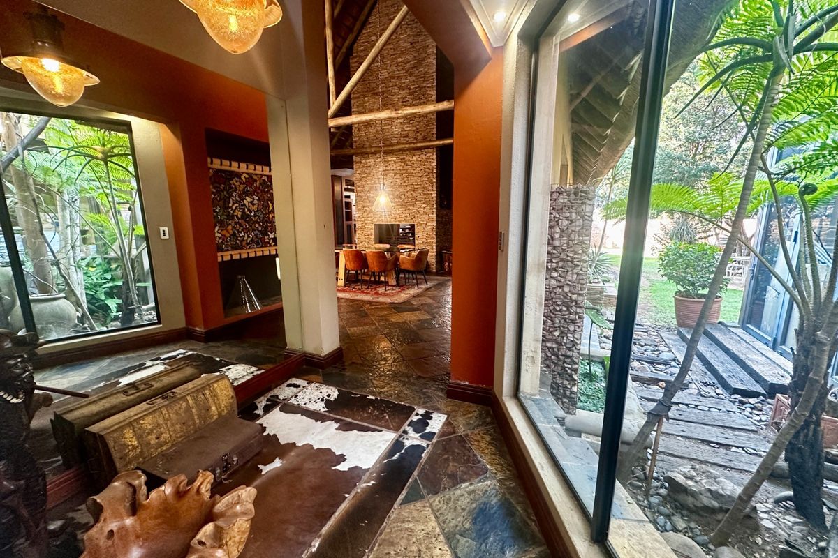 Spacious living area featuring natural slate flooring, exposed timber trusses, a striking stone feature wall, and large glass doors opening to a lush garden.