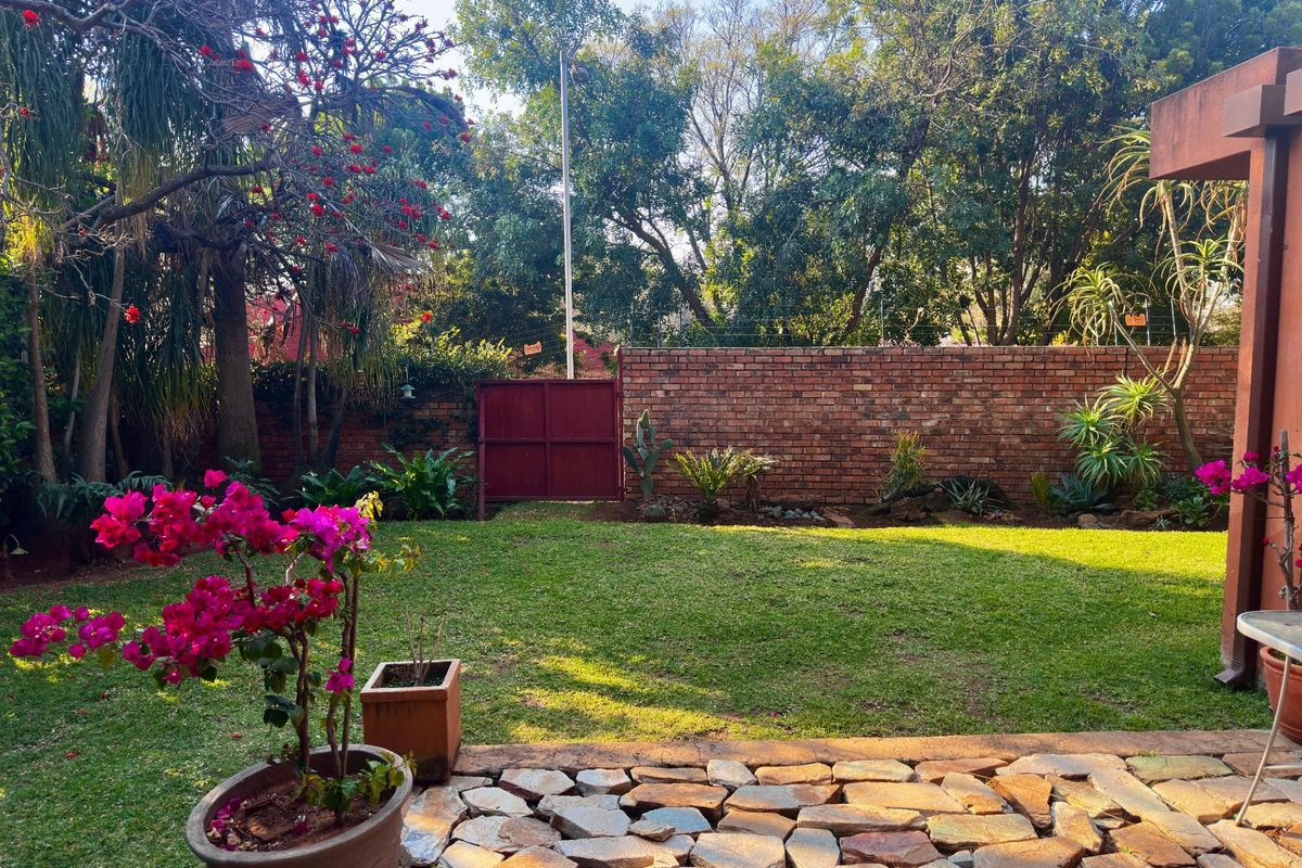 A private rear garden featuring a stone-paved patio, well-maintained lawn, and a secure brick boundary wall with mature trees.