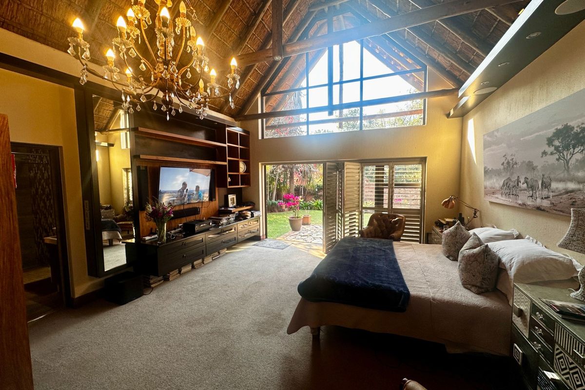 Spacious bedroom featuring a high vaulted thatched ceiling with exposed timber trusses, built-in cabinetry, and large glass doors opening to a private garden.