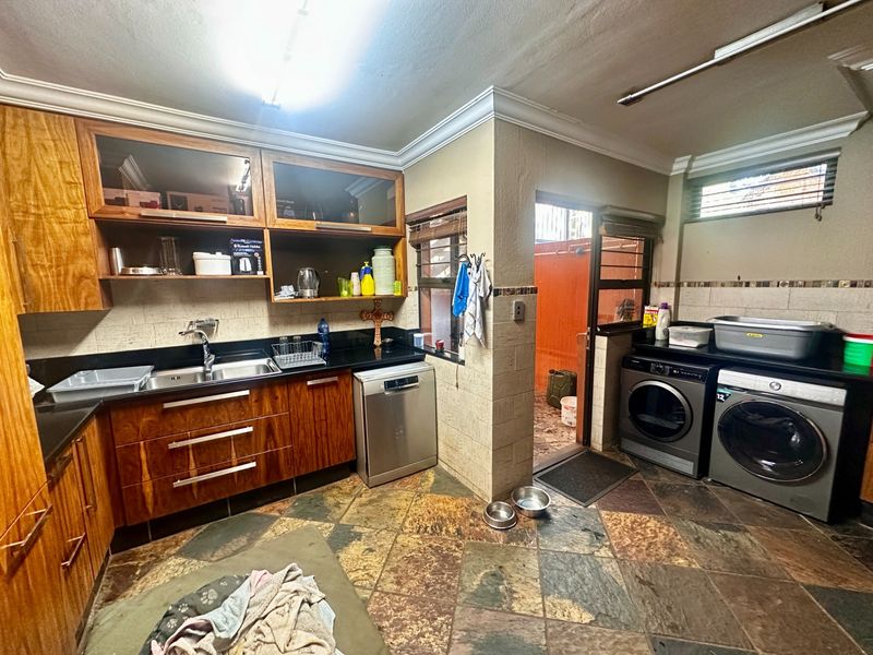 Functional laundry area featuring built-in wooden cabinetry, granite countertops, stainless steel sink, and durable tiled flooring with direct access to an outdoor space.