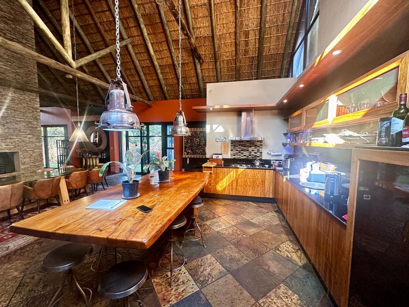 Spacious open-plan kitchen and dining area featuring a high thatched roof with exposed timber trusses, slate flooring, and modern built-in cabinetry.