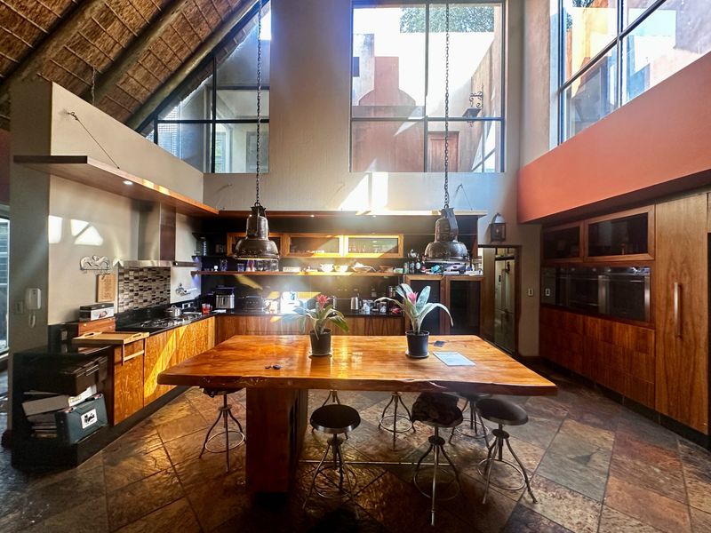 Spacious kitchen featuring high thatch ceilings, large windows, custom wooden cabinetry, stone countertops, and integrated appliances with a central wooden island.