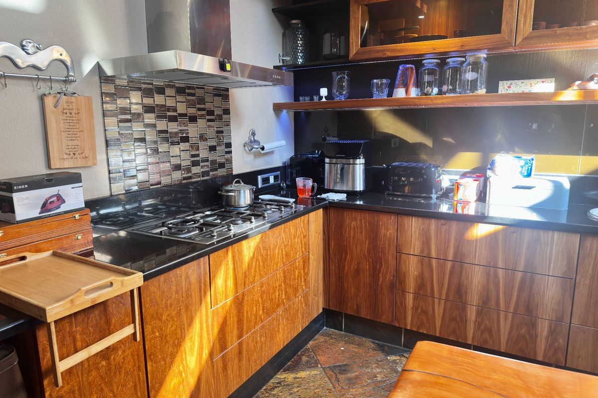 A well-appointed kitchen featuring warm wooden cabinetry, sleek black granite countertops, a gas hob with stainless steel extractor, and decorative tiled splashback.