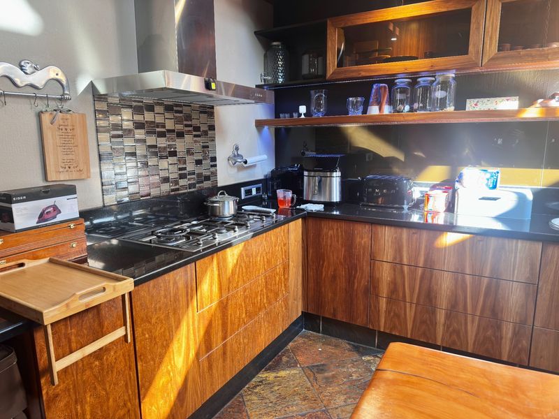 A well-appointed kitchen featuring warm wooden cabinetry, sleek black granite countertops, a gas hob with stainless steel extractor, and decorative tiled splashback.