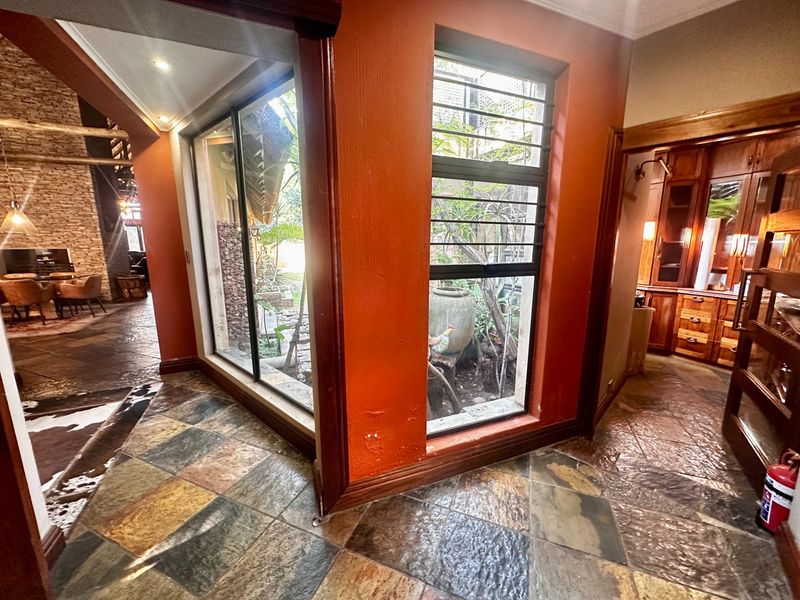 A tiled hallway featuring timber-framed windows with security bars, connecting to adjacent living and storage areas with a rustic aesthetic.