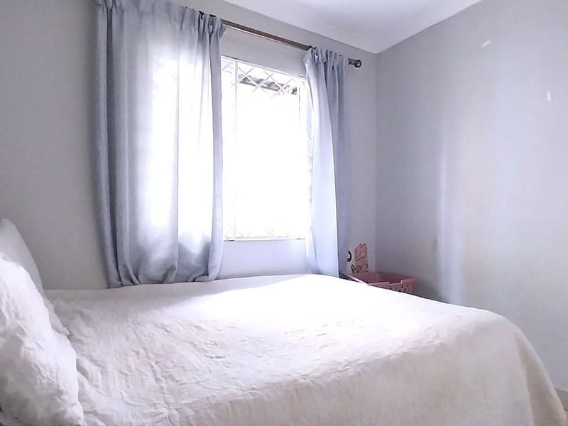 A simple bedroom featuring a window with security bars and neutral wall finishes, providing a functional and quiet sleeping space.