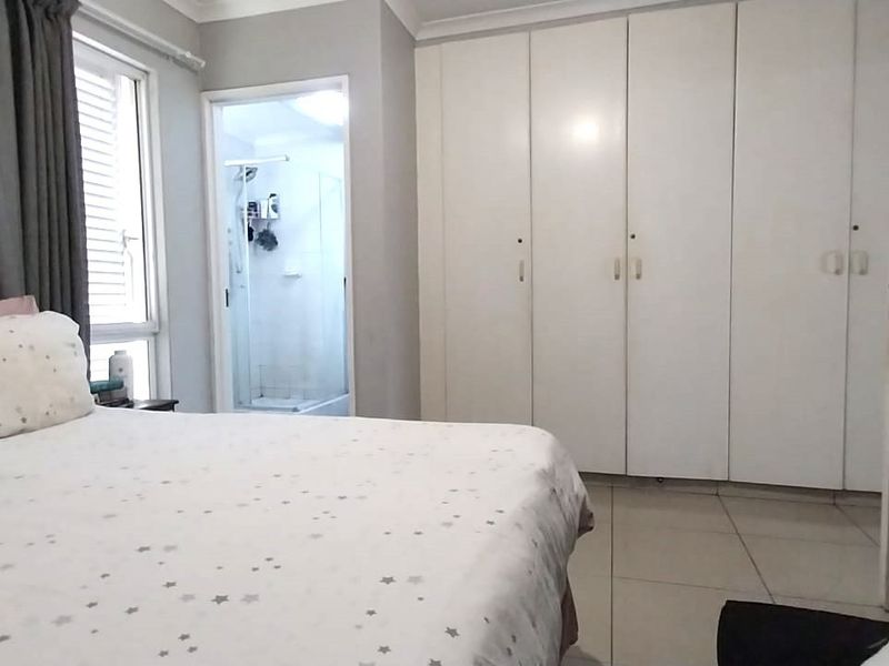 A bedroom featuring built-in cupboards, tiled flooring, and an adjoining en-suite bathroom with a shower.