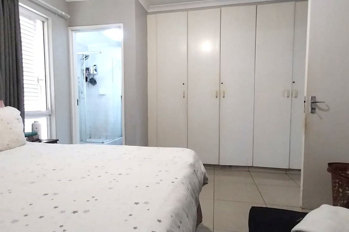 Spacious bedroom featuring neutral tiled flooring, extensive built-in cupboards, and direct access to an en-suite bathroom.