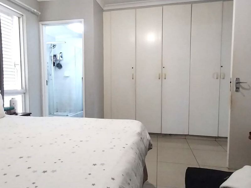 Spacious bedroom featuring neutral tiled flooring, extensive built-in cupboards, and direct access to an en-suite bathroom.