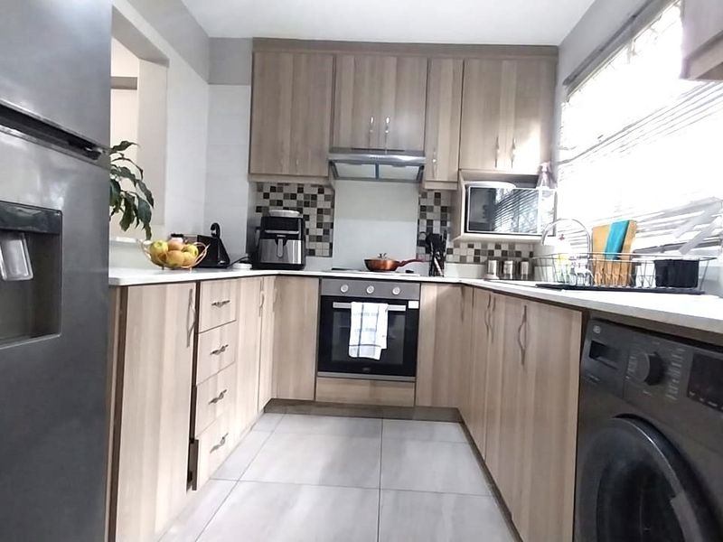 A functional kitchen featuring light wood-finish cabinetry, tiled flooring, a built-in oven with extractor fan, and a tiled backsplash.