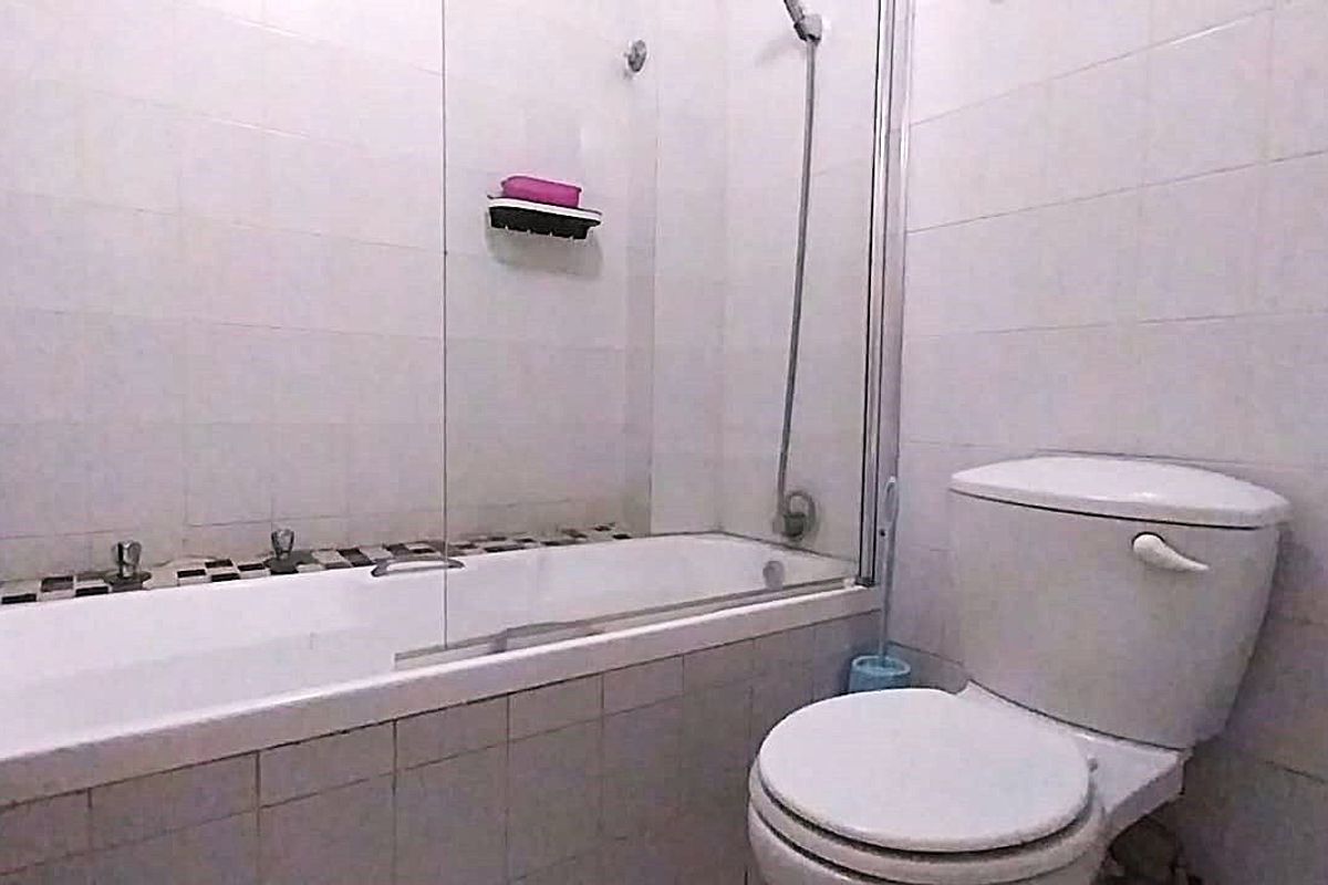 A functional bathroom featuring a bathtub with a glass shower screen, tiled walls, and a standard toilet.