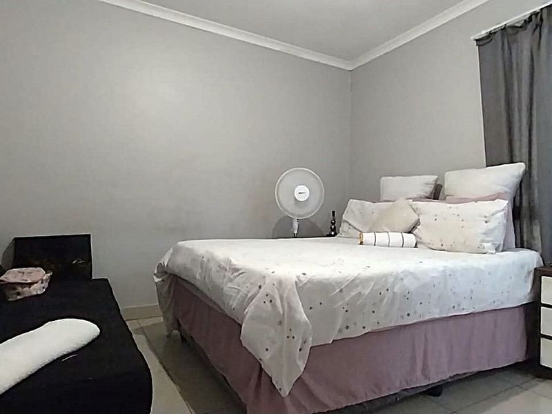 A functional bedroom featuring tiled flooring, neutral wall finishes, and a large window allowing for natural light.