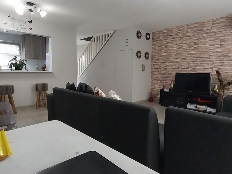 Open-plan living and dining area featuring a stone-cladding accent wall, split-system air conditioning, and a breakfast bar overlooking the kitchen.
