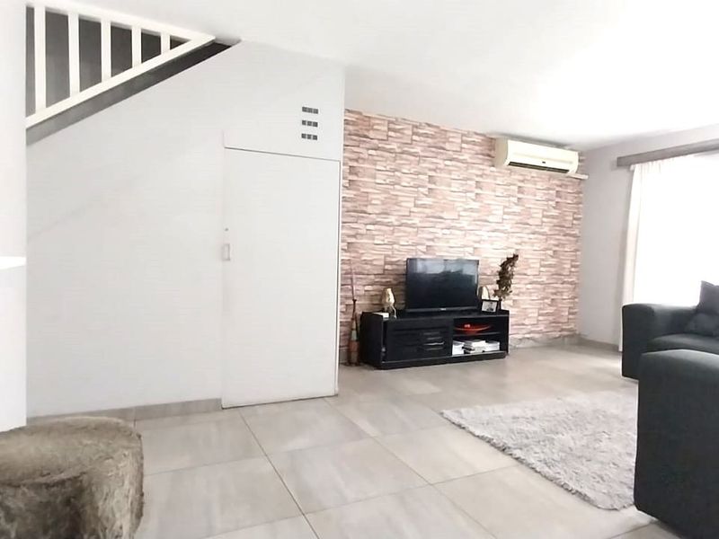 A living room featuring tiled flooring, a staircase, and a decorative feature wall with an integrated air conditioning unit.
