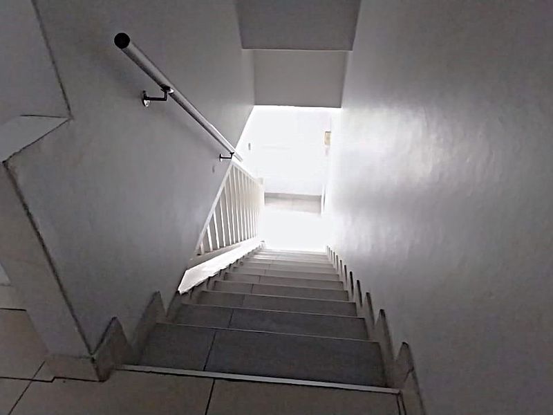 A view looking down a tiled staircase featuring a metal handrail, leading to a lower level.