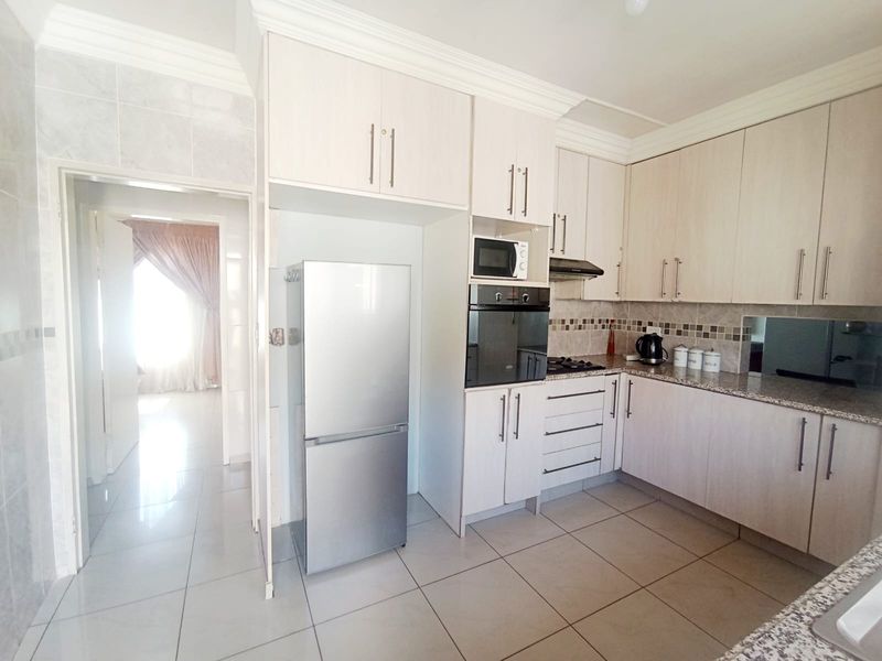 A functional kitchen featuring light-toned built-in cabinetry, granite countertops, a built-in oven, and tiled flooring, with an adjacent doorway leading to another room.