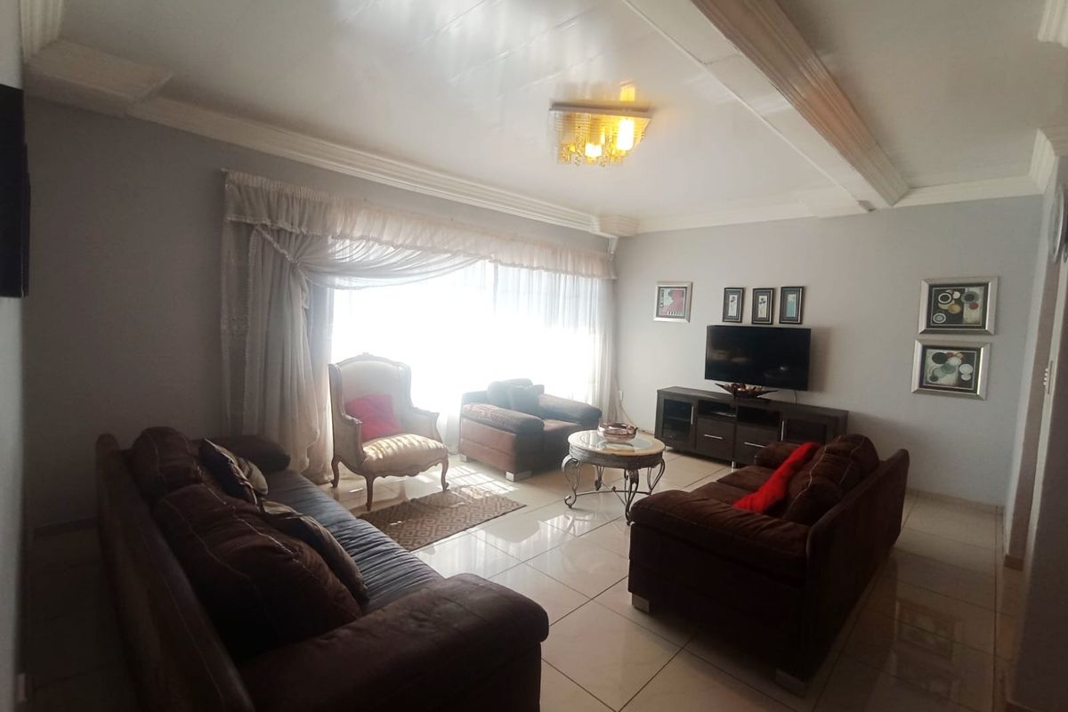 A spacious living room featuring polished tiled flooring, decorative ceiling molding, and a central light fixture, creating a comfortable and well-maintained living space.