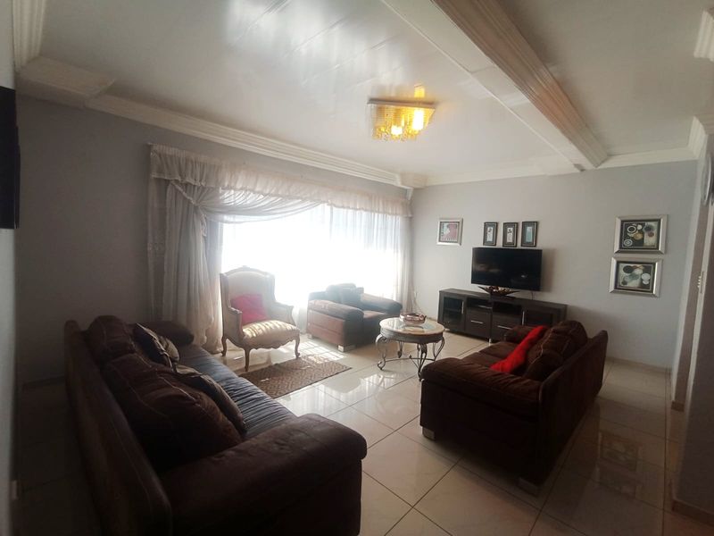 A spacious living room featuring polished tiled flooring, decorative ceiling molding, and a central light fixture, creating a comfortable and well-maintained living space.