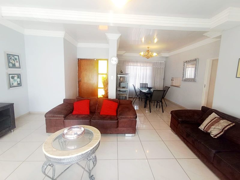 Spacious open-plan living and dining area featuring neutral tiled flooring, crown molding, and ample natural light from the rear window.